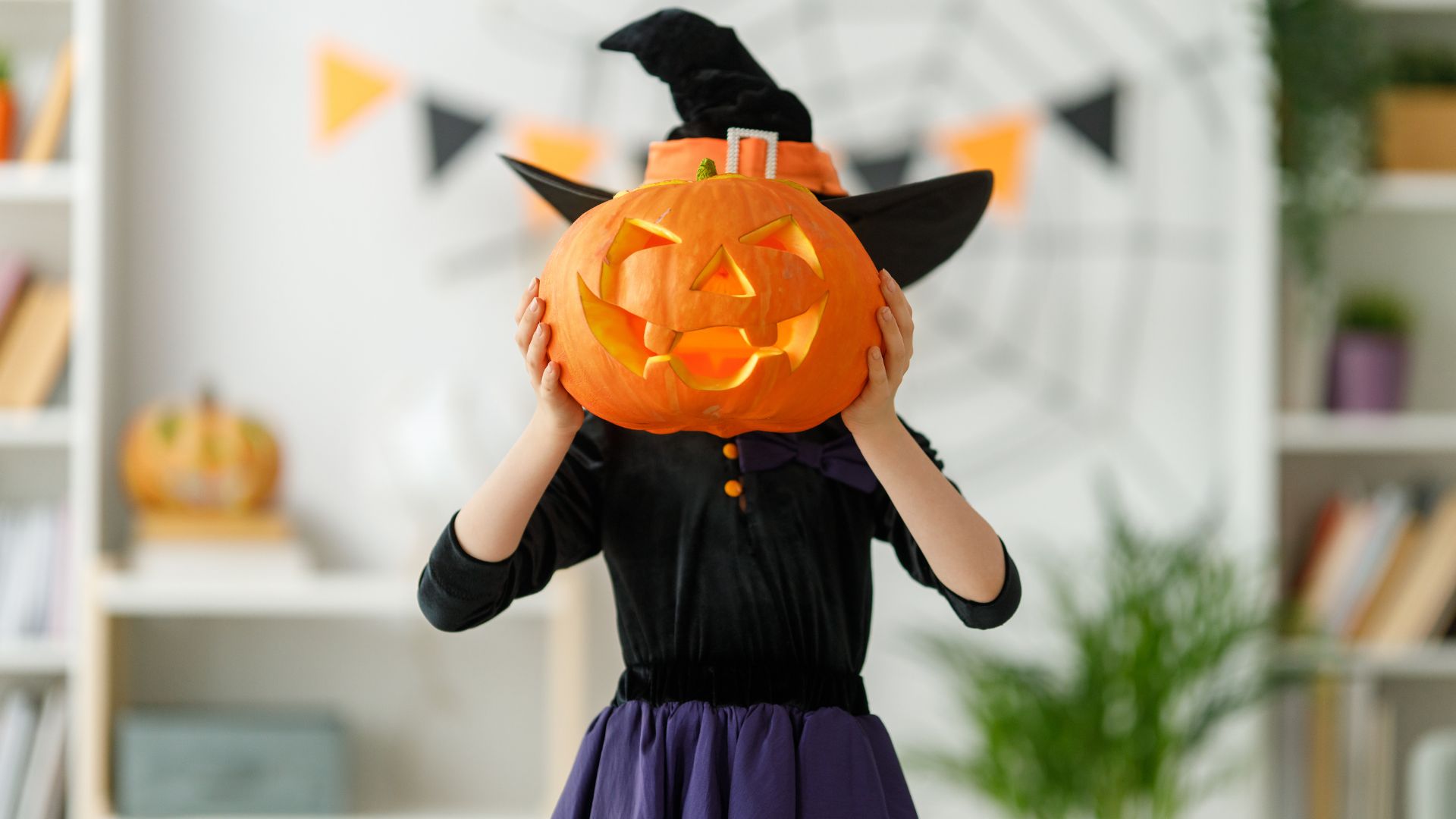 Girl in witch costume holding halloween pumpkin